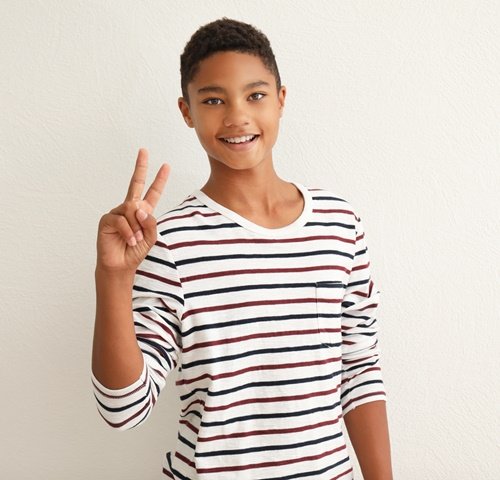 Schwarzer Junge zeigt "Peace" und lächelt in die Kamera Quiz über Jungen in der Pubertät