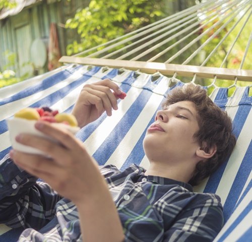 Junge isst Obst und liegt in einer Hängematte Online-Kurs zu Gesundheit in der Pubertät: Schlafen, Hygiene, Stress